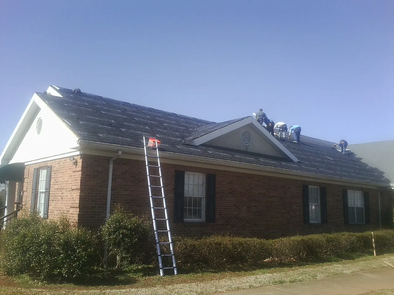 Crew tearing shingles off a brick ranch roof with a ladder set — Metal Roof Repair work by our crew in Conestoga