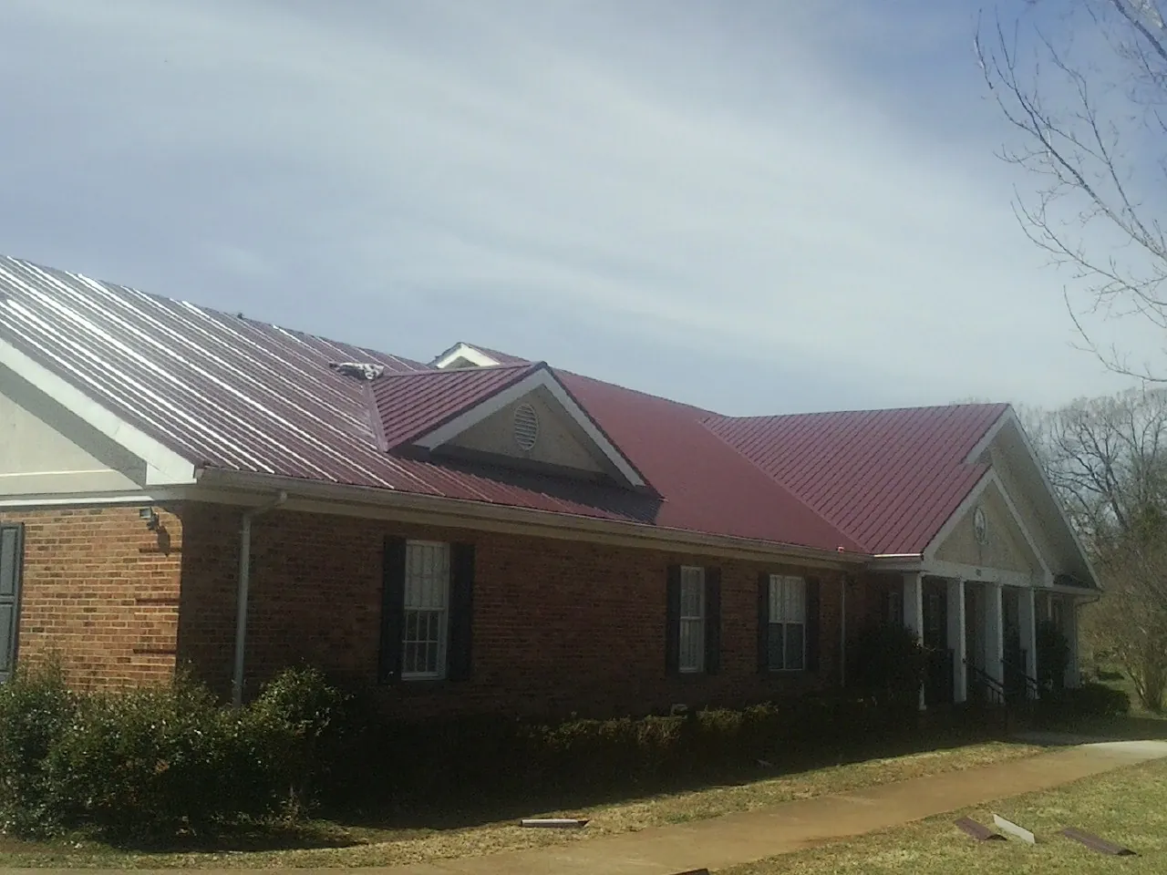 Red metal roof with gabled entries on a long brick building, from a Hail Damage Roof Repair job in Conestoga