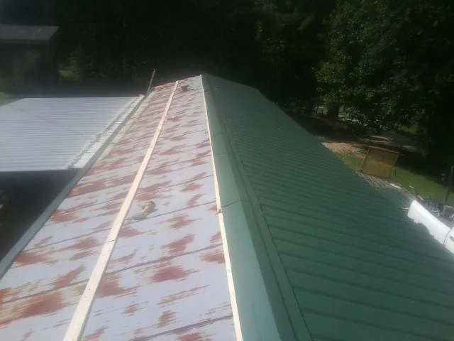 Old rusted panels beside newly installed green metal roofing — Wind Damage Roof Repair by Roofing Brothers in Conestoga