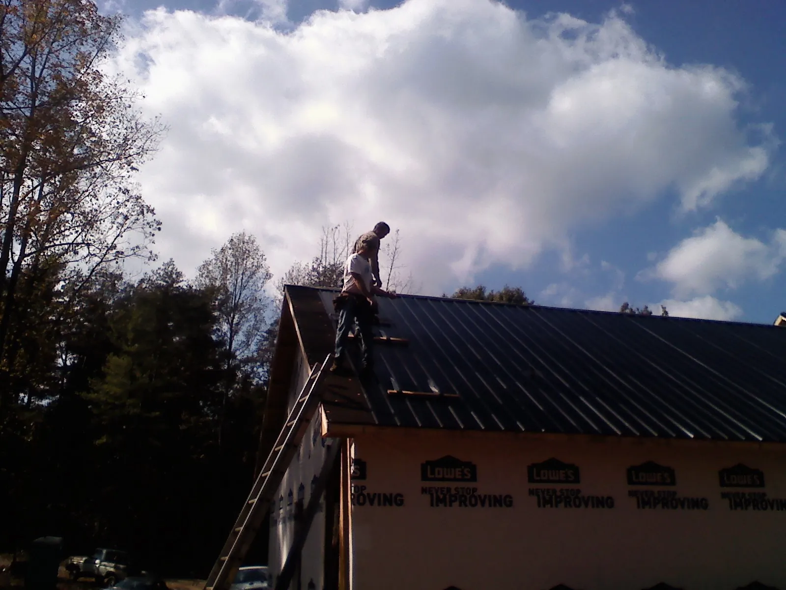 Roofer fastening dark metal panels high against a cloudy sky, from a Roof Inspection job in Conestoga