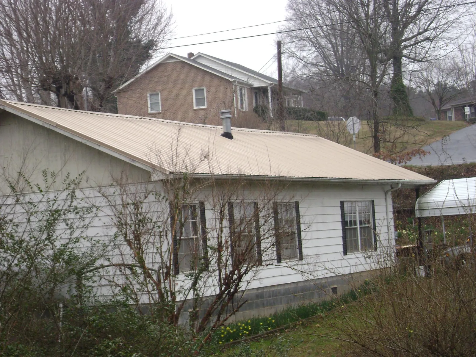 Tan metal roof on a white sided house set into a hillside — Commercial Roofing by Roofing Brothers in Conestoga